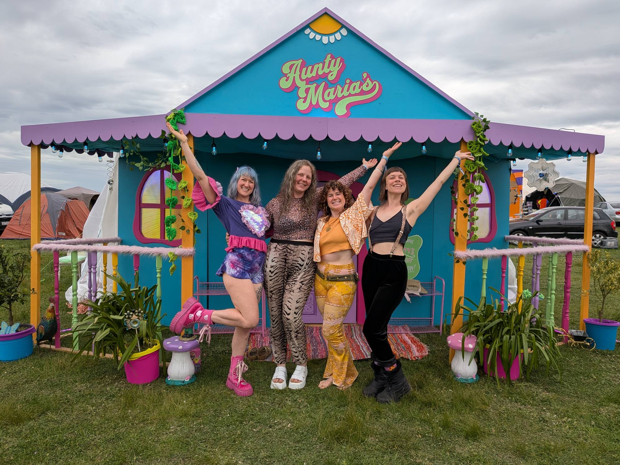 Four members of the Aunty Maria’s crew posing with arms raised on the front porch