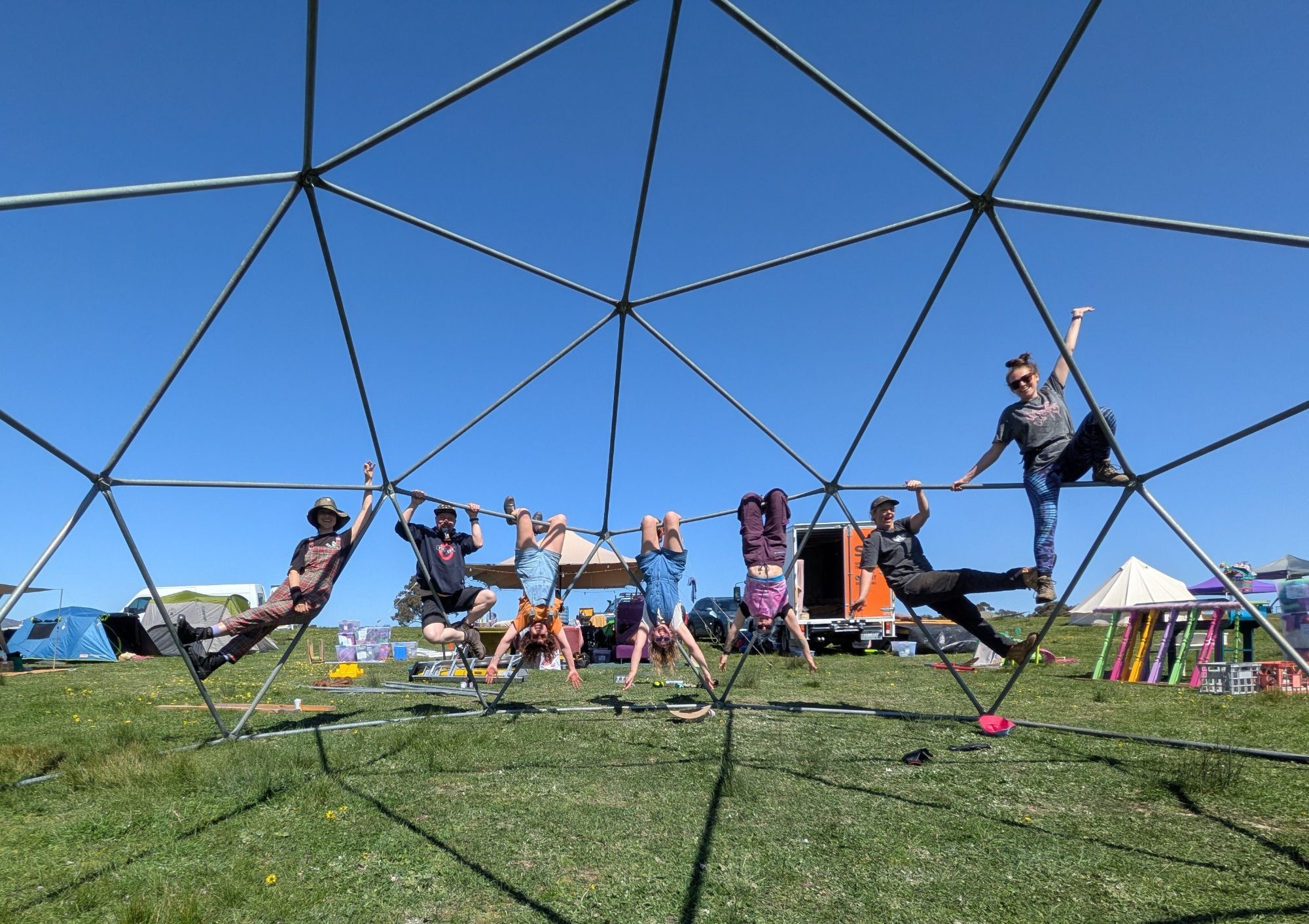 Seven crew members hanging upside down and climbing on a geodesic dome frame mid-build