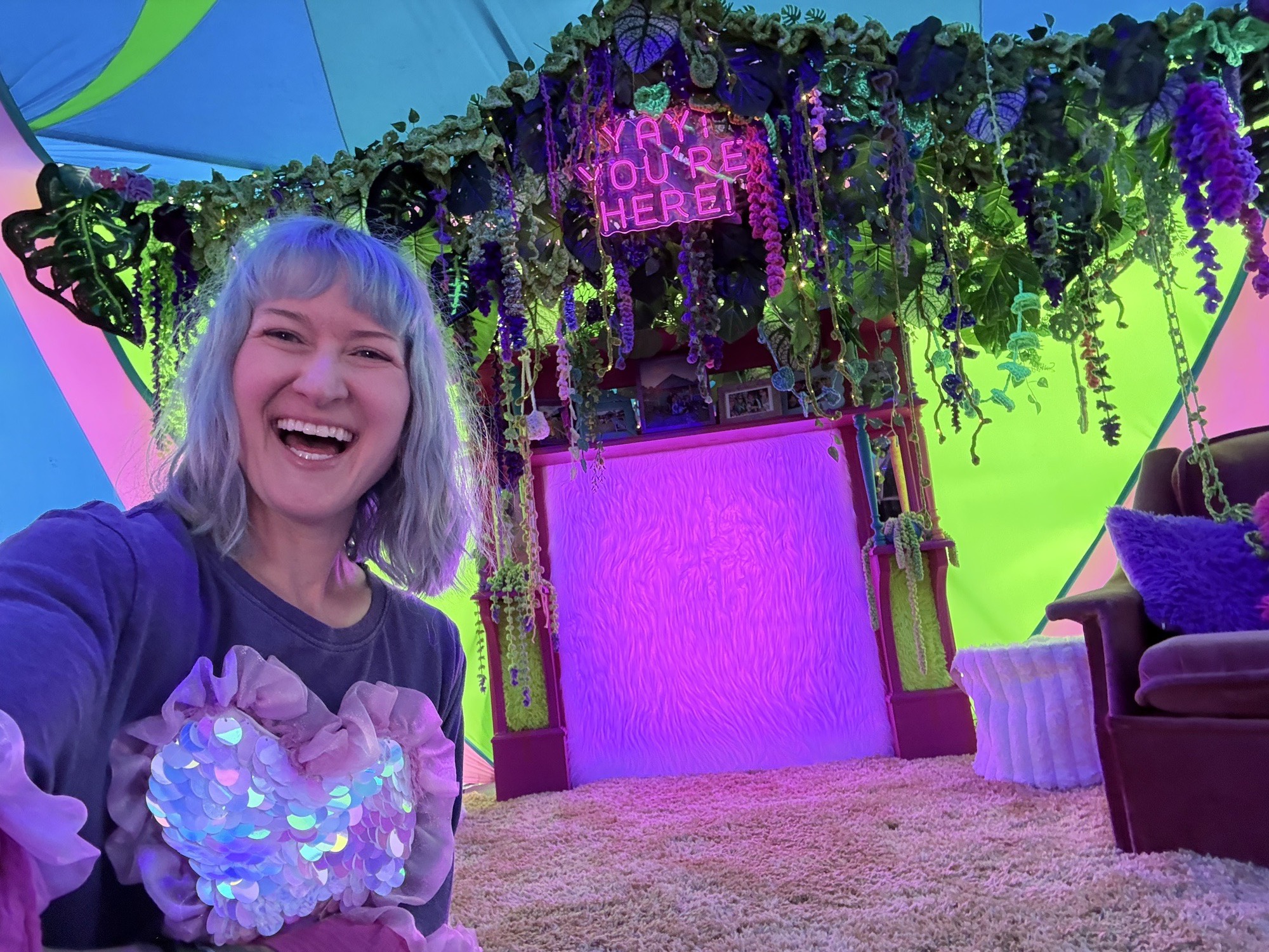 Jess laughing in a selfie in front of the crochet-draped fireplace and its neon ‘Yay! You’re here!’ sign
