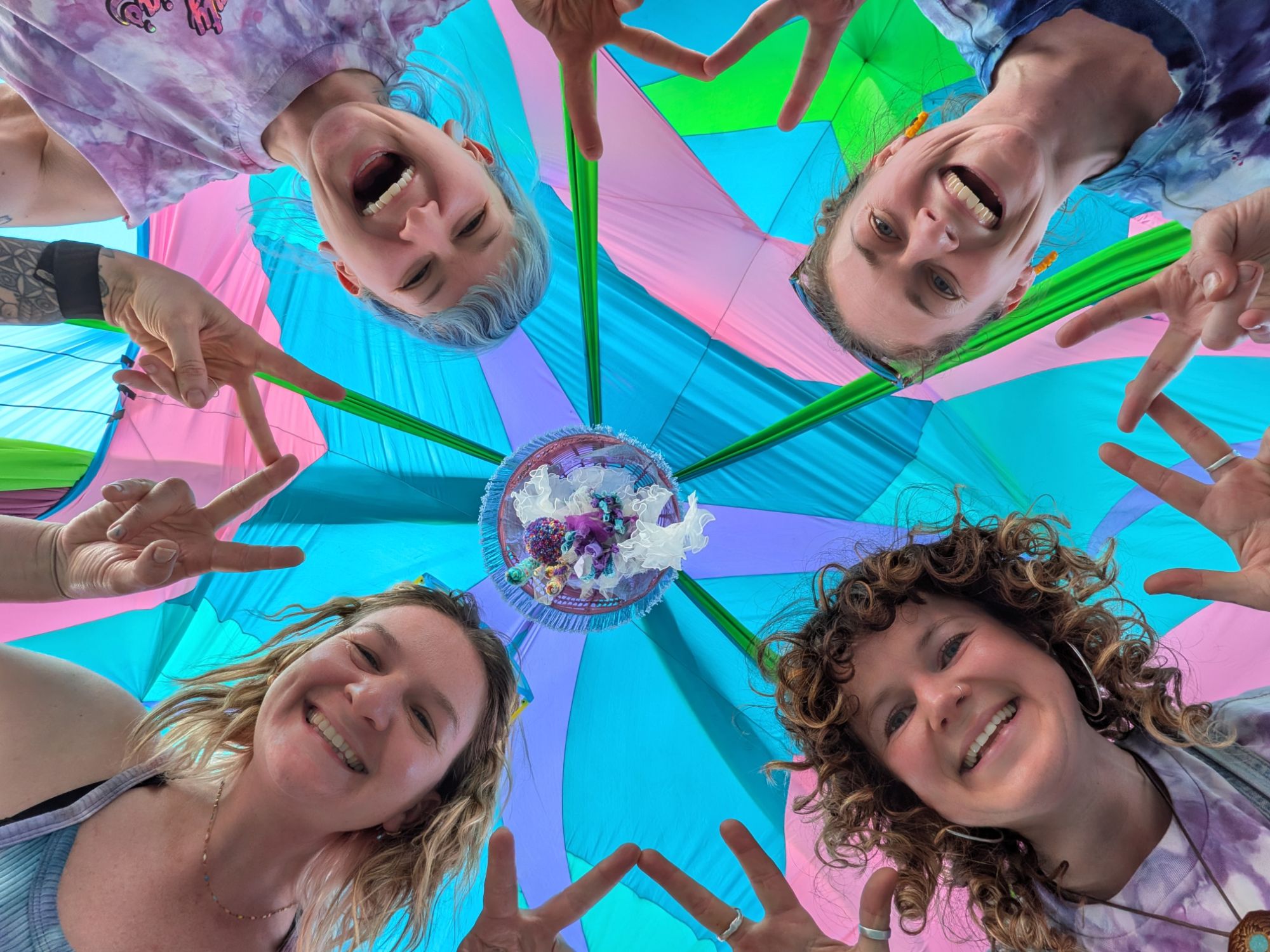 Four crew members looking down into the camera, framed by a pink, teal and green tent canopy