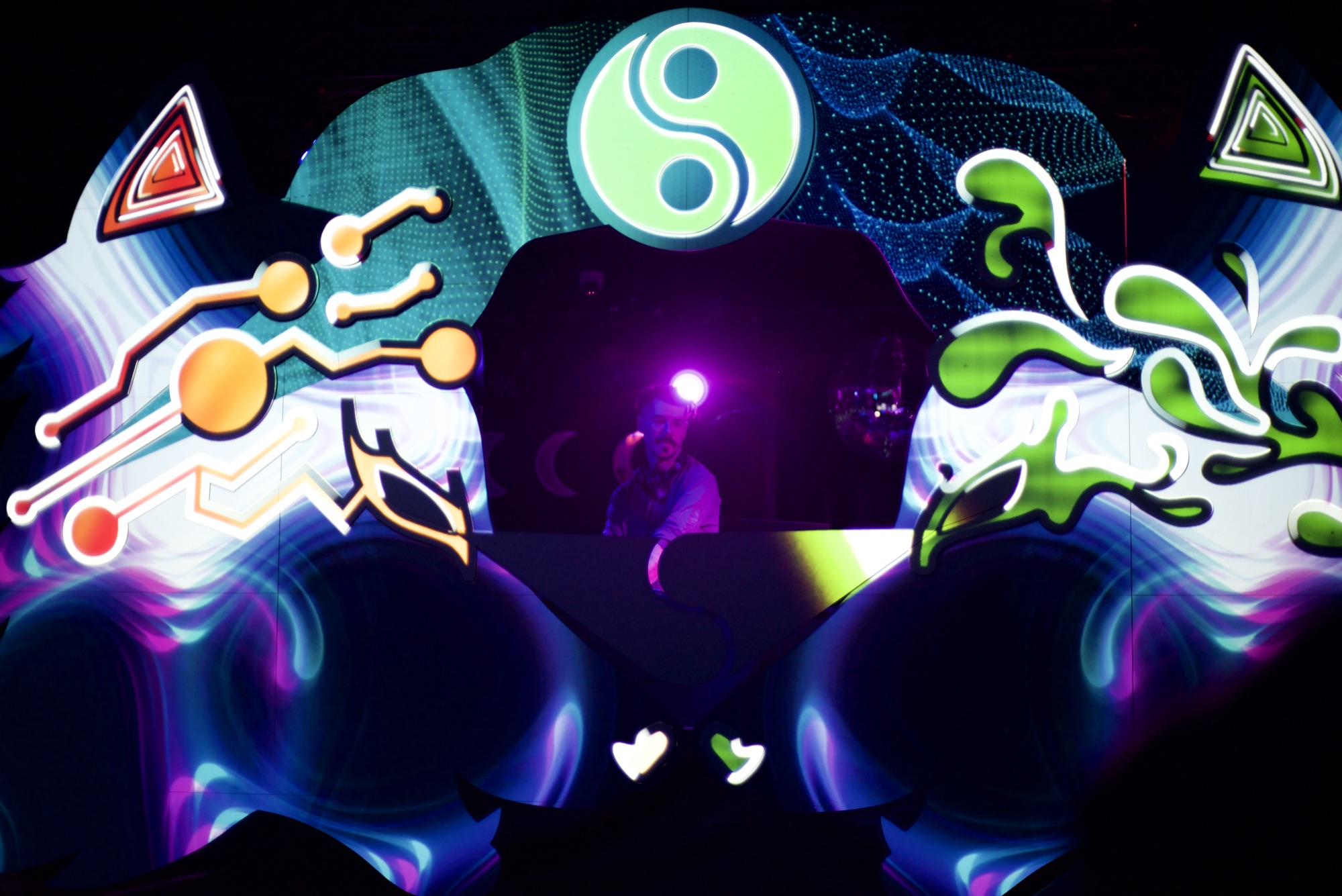 A symmetrical UV stage split into two halves, circuit shapes on one side and organic splashes on the other, under a glowing yin-yang