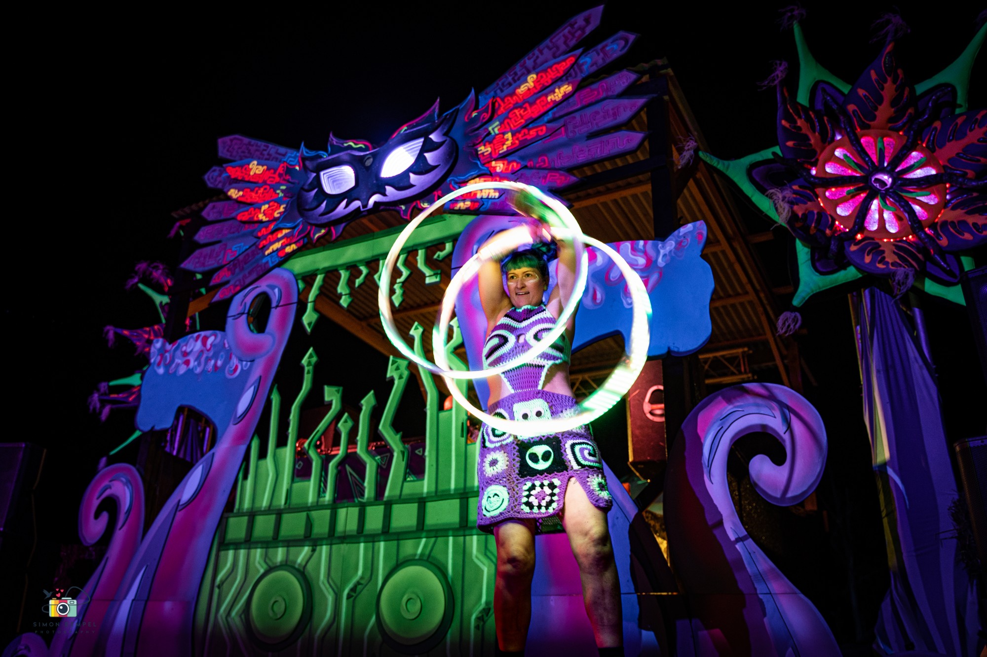 Jess hooping in a crochet alien outfit in front of the winged-mask stage under UV light