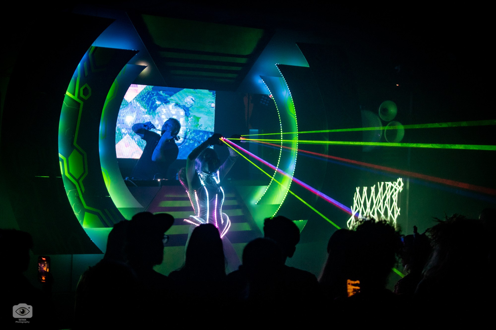 A performer in an LED corset firing lasers from her hands in front of the circular portal stage