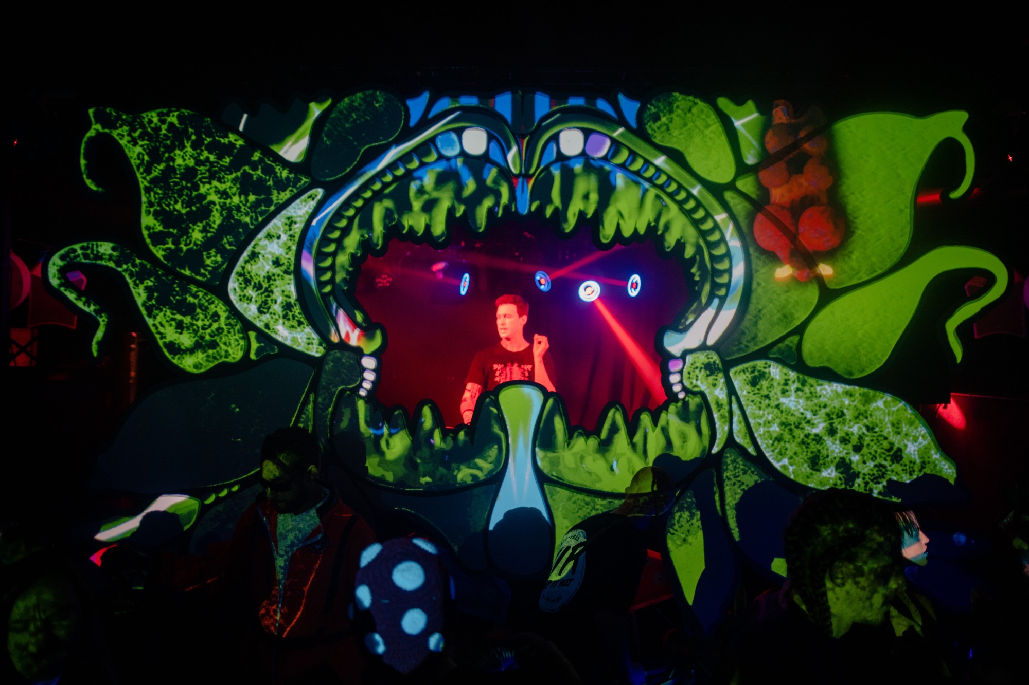 The DJ framed inside the gaping jaws of a giant carnivorous plant stage, lit with green projection mapping
