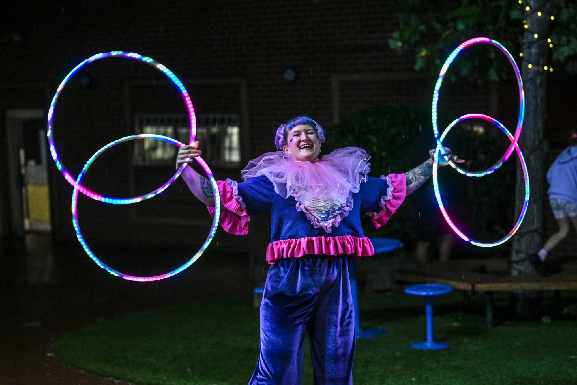 Jess at night holding two pairs of glowing hoops out to each side, wearing a pink tulle ruff