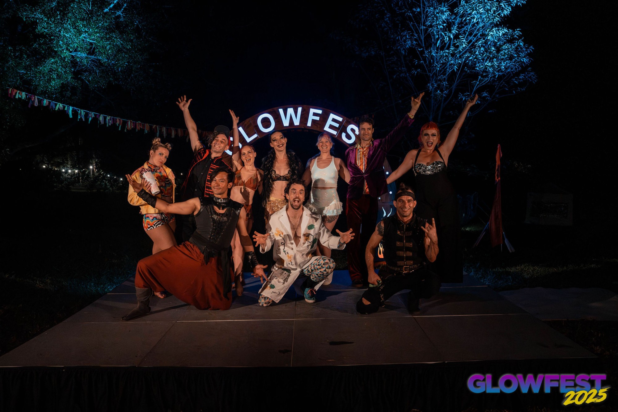 The Glowfest 2025 performer cast posing together under the lit Glowfest arch
