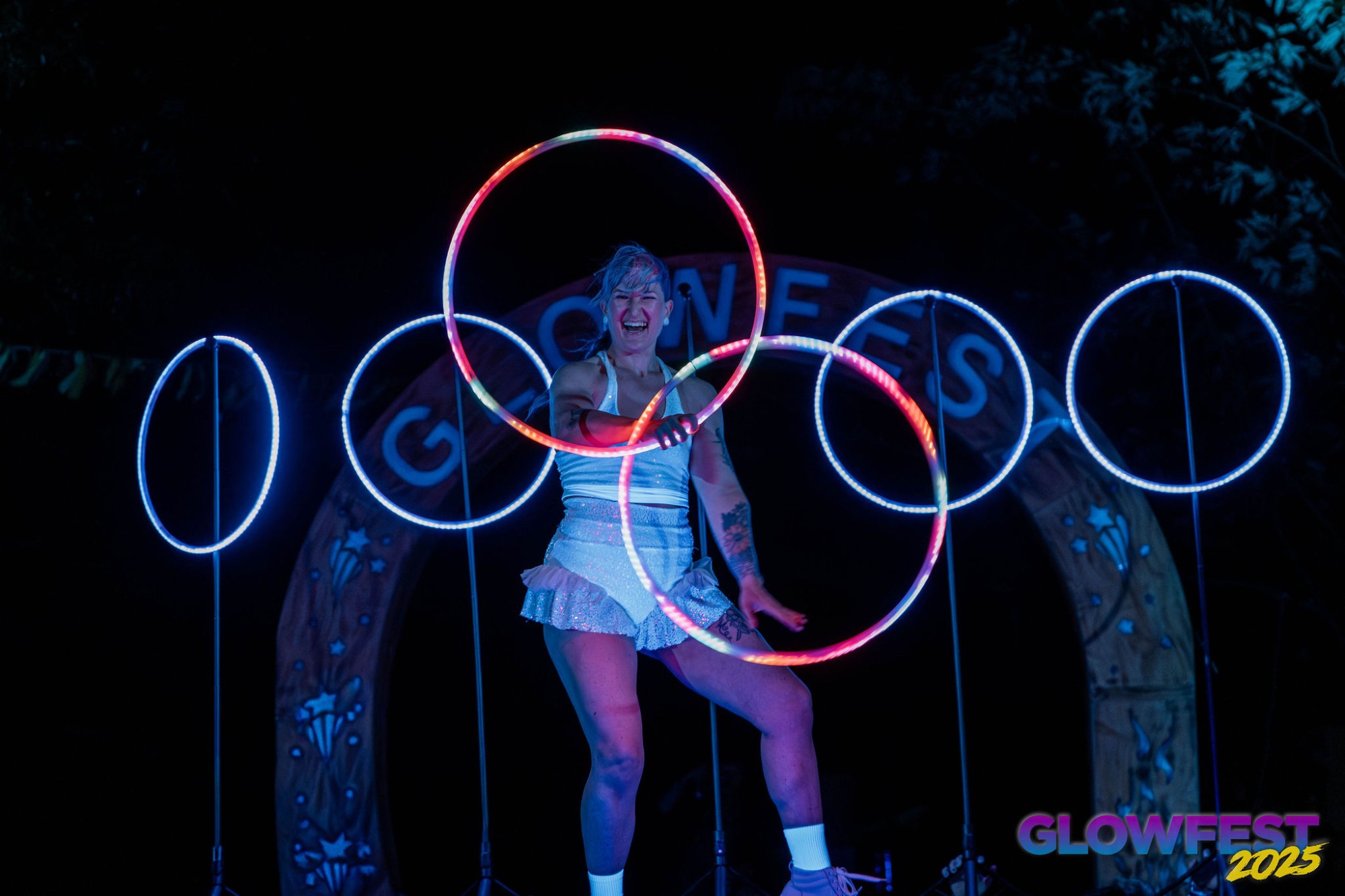 Jess laughing mid-act with two LED hoops in front of a row of glowing hoops and the Glowfest arch