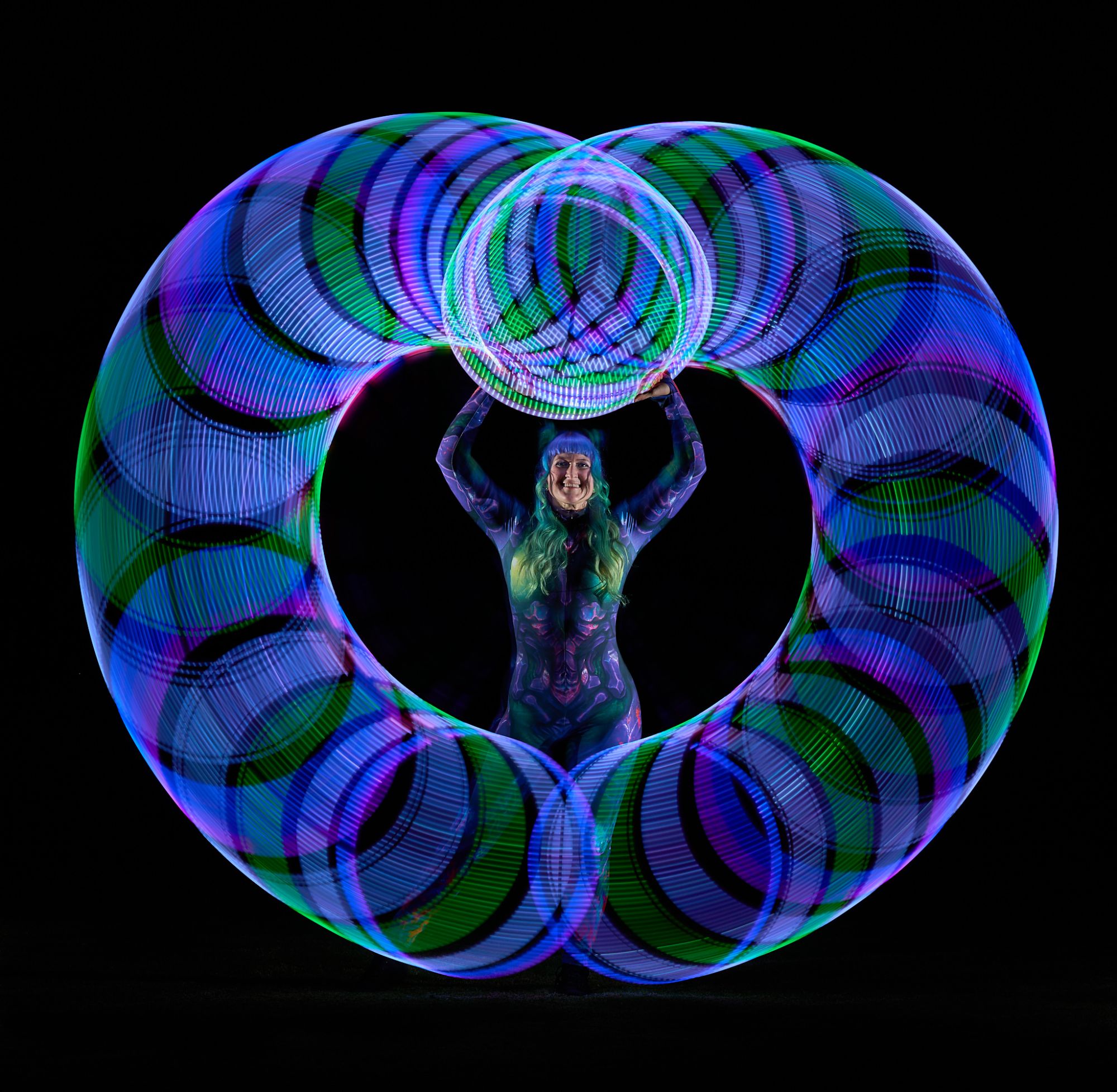 Long-exposure light painting: LED hoop trails forming a huge blue and green ring around Jess