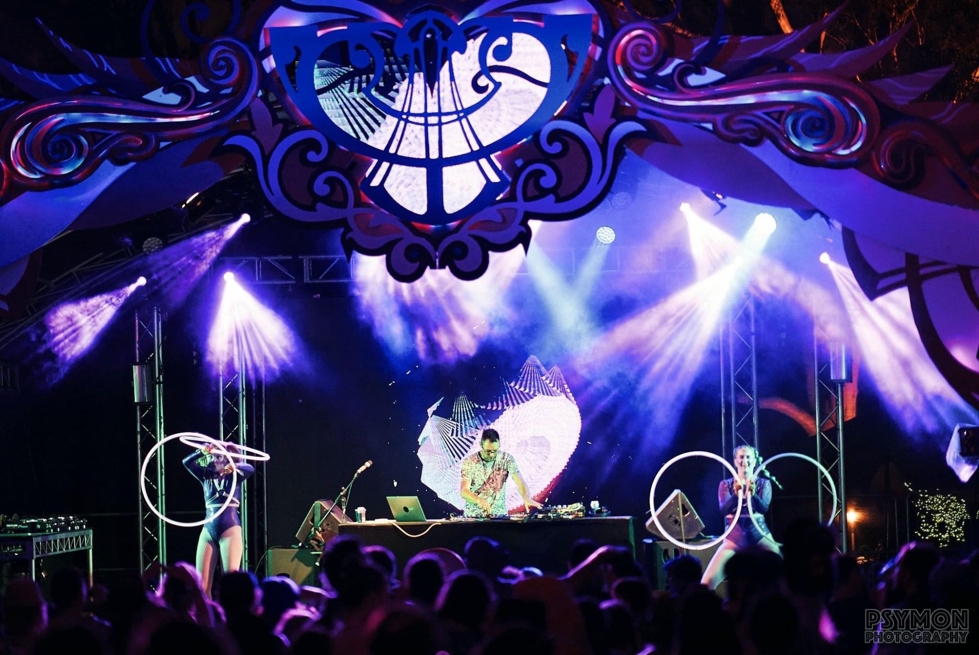 Two hoopers performing either side of the DJ on a festival main stage under an ornate lit canopy