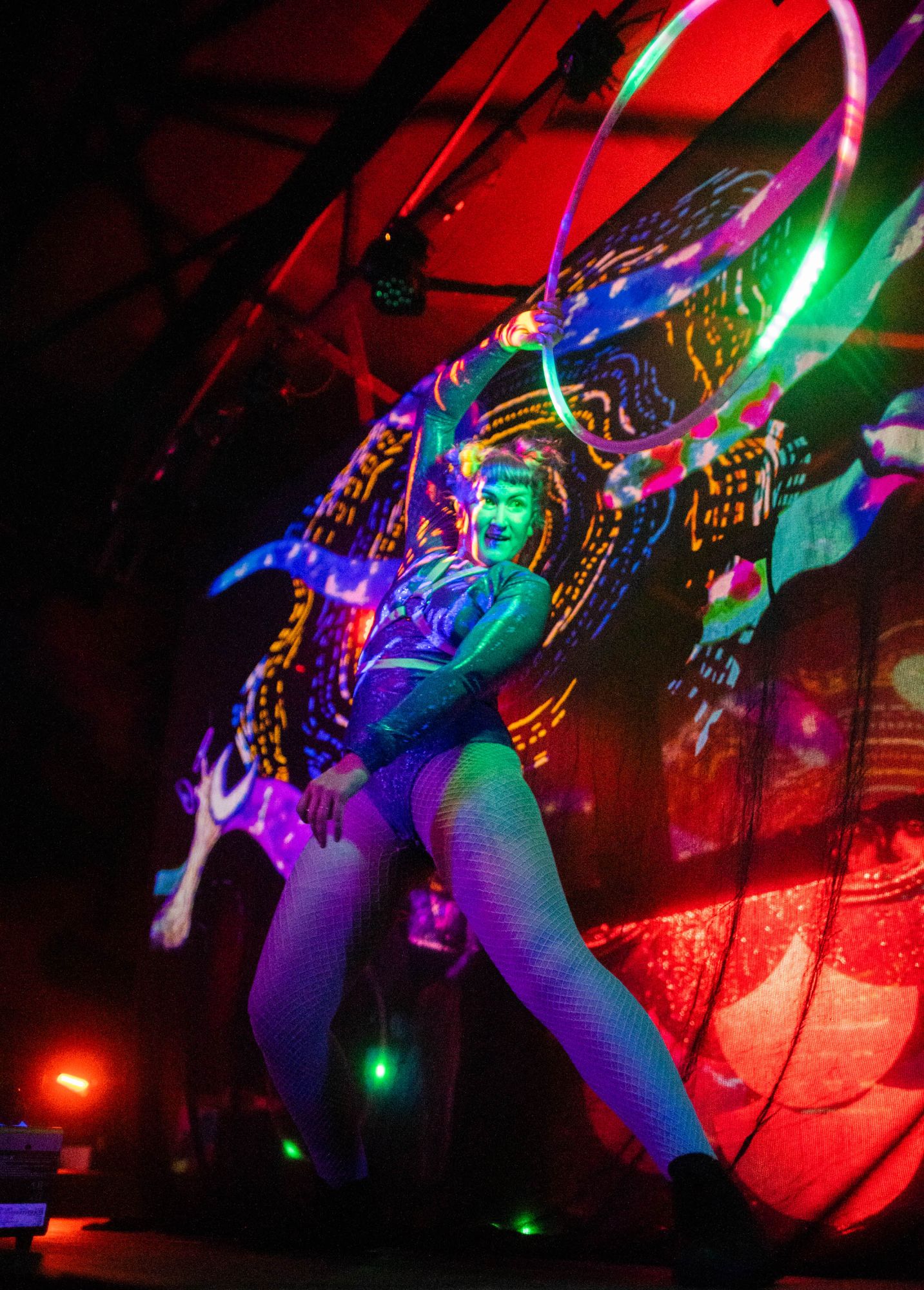 Jess mid-move with an LED hoop raised against swirling projection-mapped visuals