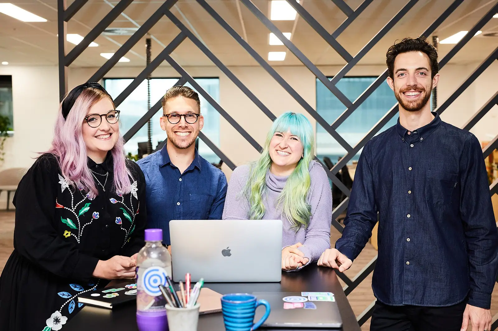 The Plan product team smiling around a high table with their laptops.