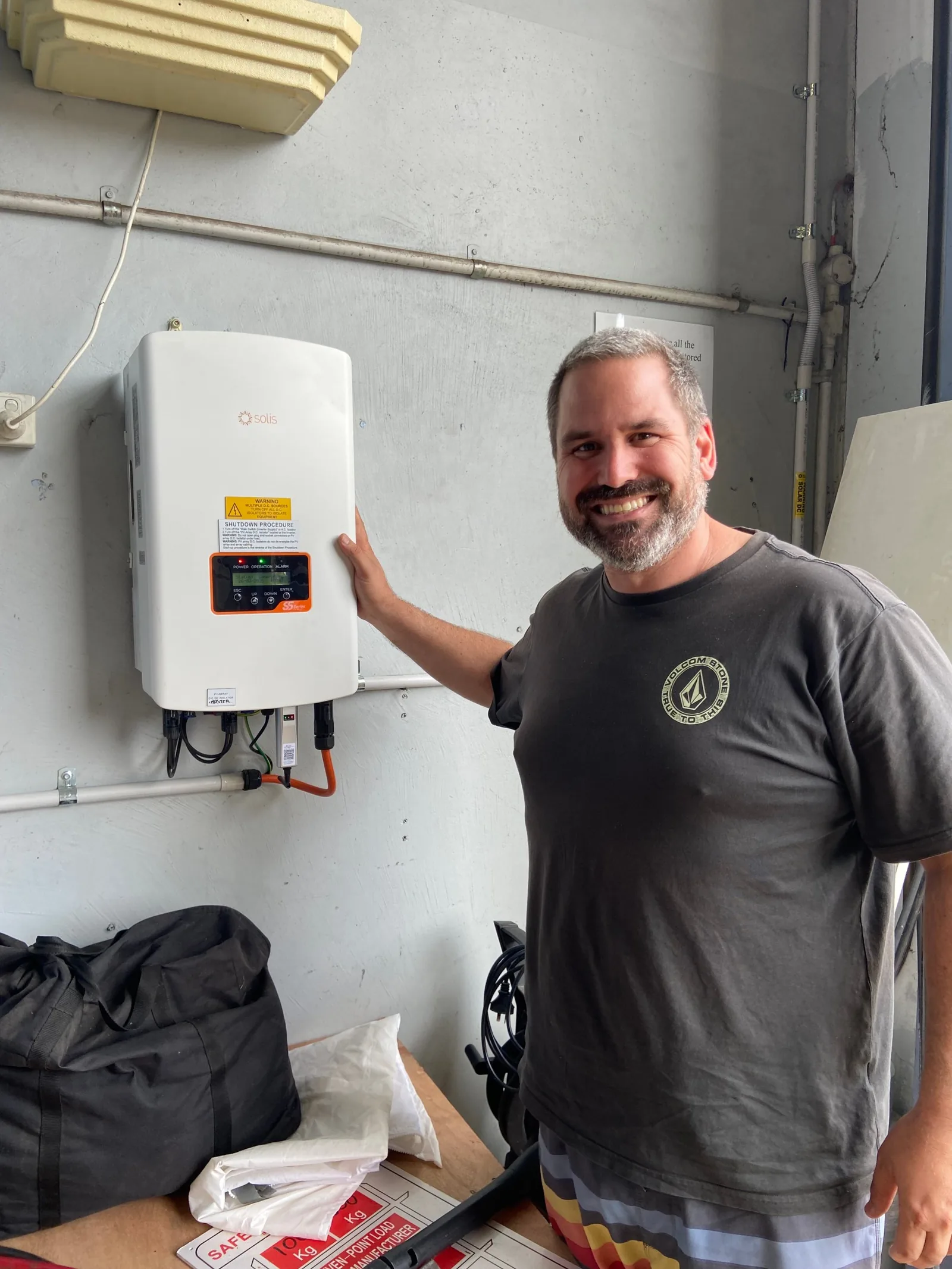 James smiling with his hand on the newly installed solar inverter.