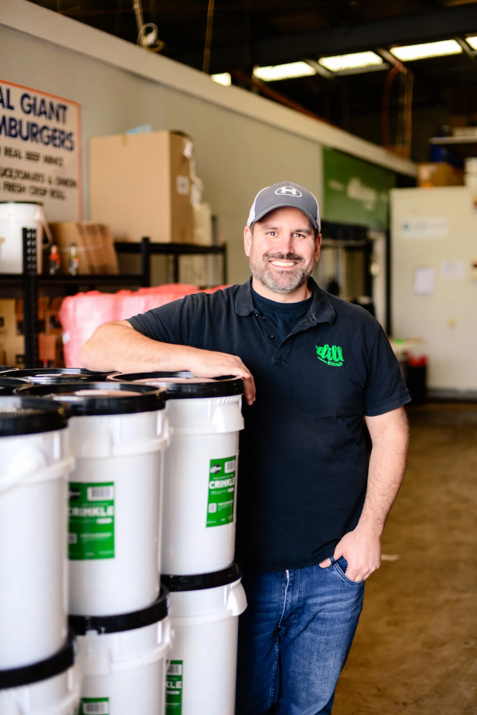James Barbour, founder of Dillicious, smiling beside stacked pickle buckets at The Brinery.